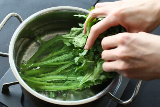 春菊の葉の部分を手で持ちながら、茎の方を湯に浸す