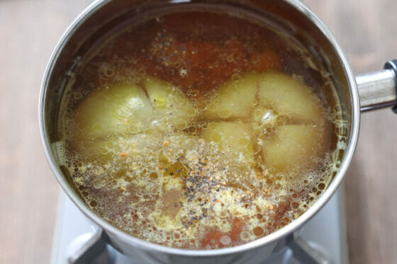 ベーコンが入った鍋に玉ねぎ・コンソメ・水・胡椒を加える