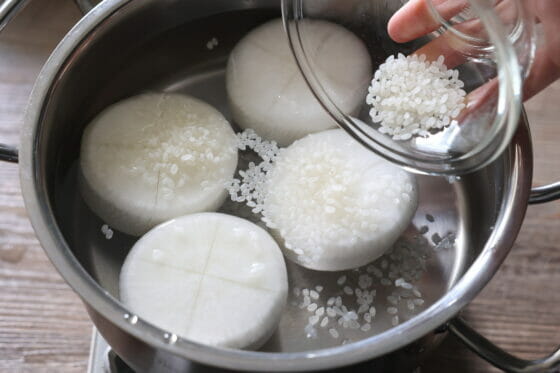 隠し包丁を入れた面を上にして大根を鍋に入れて米を加える