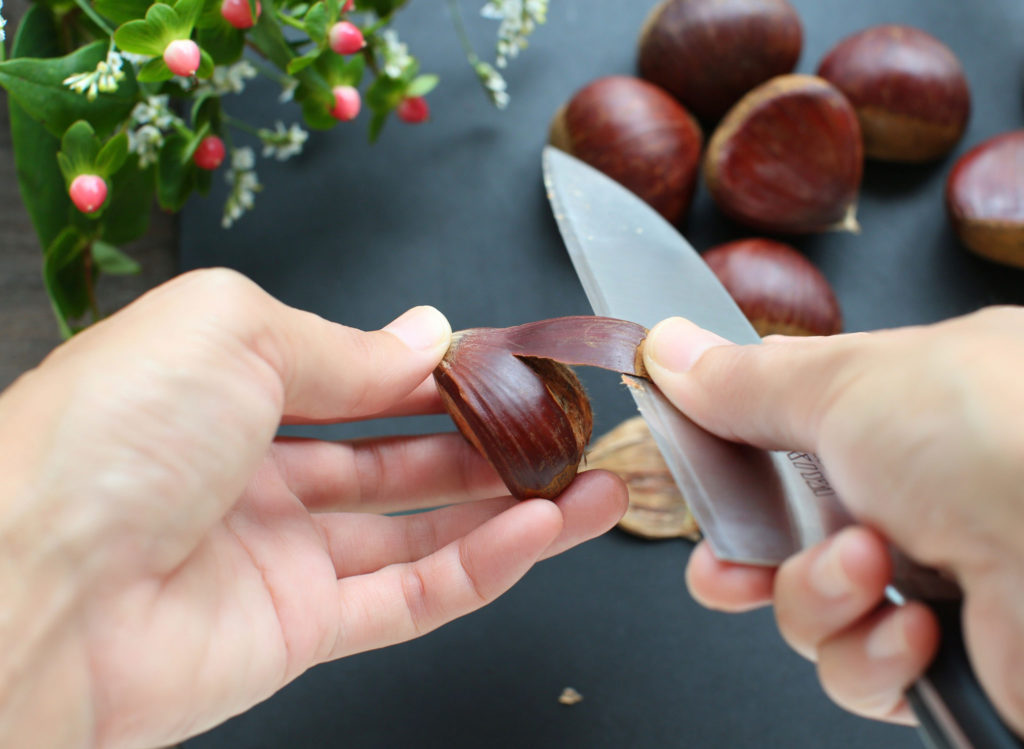 Chestnuts with tough outer skins being peeled on a wooden surface
