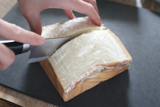 ラップで包んだサンドイッチを包丁で切る