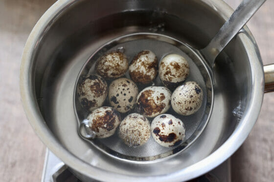 うずらの卵を網杓子ごと湯に入れる