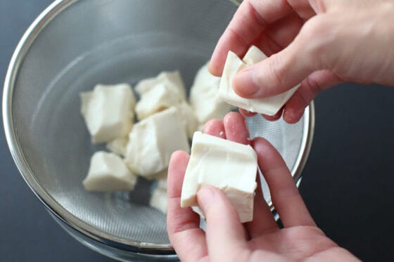 豆腐を手でちぎってザルに上げ、水切りをする
