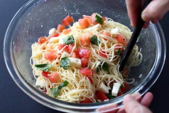 トマトが入ったボールにパスタとチーズとバジルの葉を加えて和える