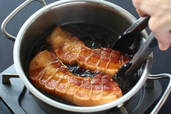 トングで煮豚を裏返して煮汁をなじませる