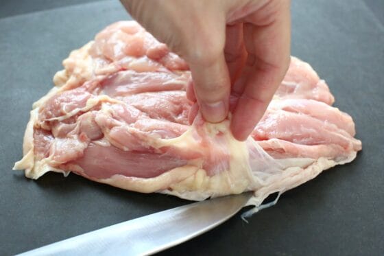 鶏もも肉の脂と筋を包丁で取り除いて下処理をする