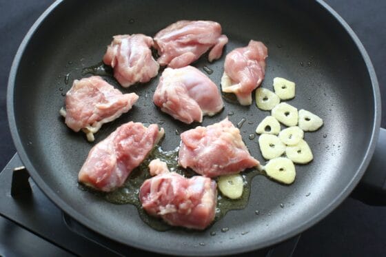 にんにくをフライパンの端に寄せて鶏肉を並べる
