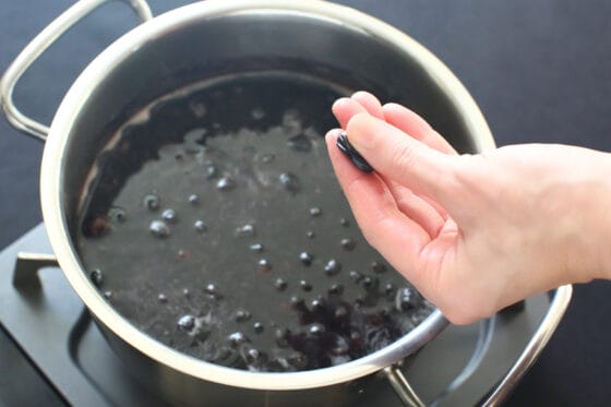 柔らかくなった黒豆を指で押して茹で加減を確認する
