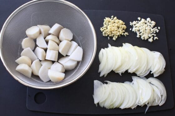 里芋をザルにあげて玉ねぎとニンニクと生姜を切る