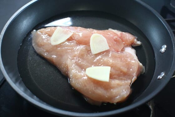 フライパンに鶏肉と酒水生姜を入れて蒸し鶏の準備をする
