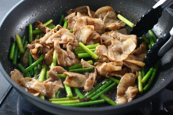 豚肉とにんにくの芽にたれを加えて絡める