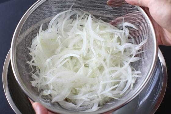 水にさらした新玉ねぎをザルに上げる
