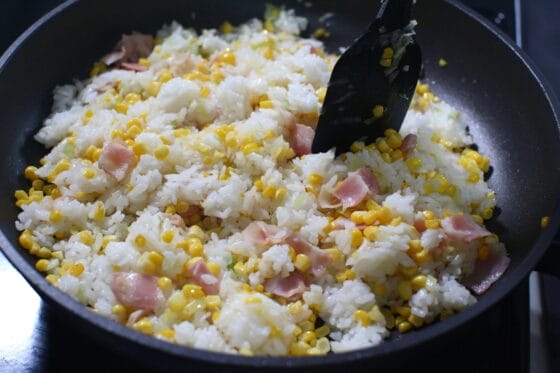 とうもろこしとベーコンに温かいご飯を加えてほぐしながら炒める