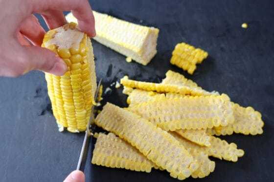 加熱したとうもろこしを立て、包丁で実を芯からそぎ落とす