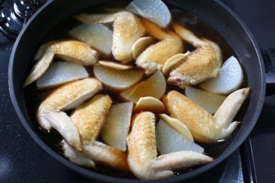 焼いた手羽先に大根と生姜、調味料、水を加えて煮立たせる