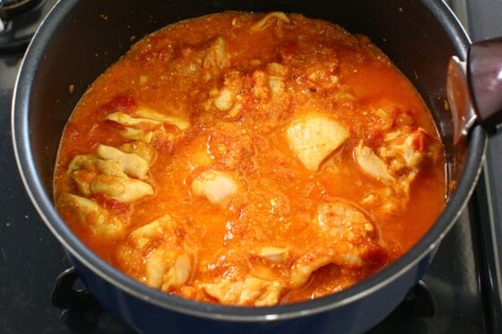 スパイスとトマトを絡めた鶏もも肉に水を加え、全体を混ぜ合わせる