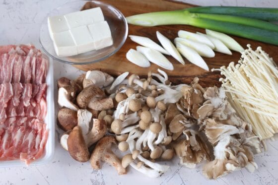 きのこ鍋の材料となるしめじ、えのき、舞茸、しいたけ、長ねぎ、豆腐、豚バラ肉を切って準備する