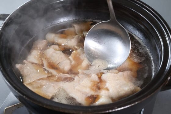きのこ鍋の豚バラ肉を煮ながら、表面に浮いてきたアクをおたまで取り除く