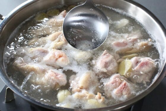 鶏肉を煮立て、スープの表面に浮いたアクをおたまで丁寧に取り除く